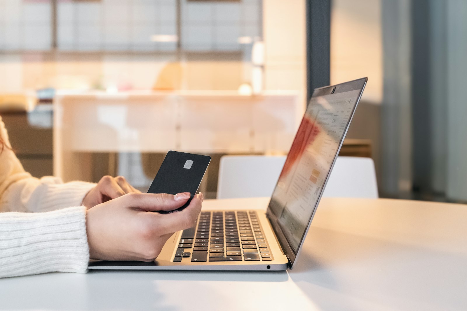 Hands holding a payment card in front of an open laptop.