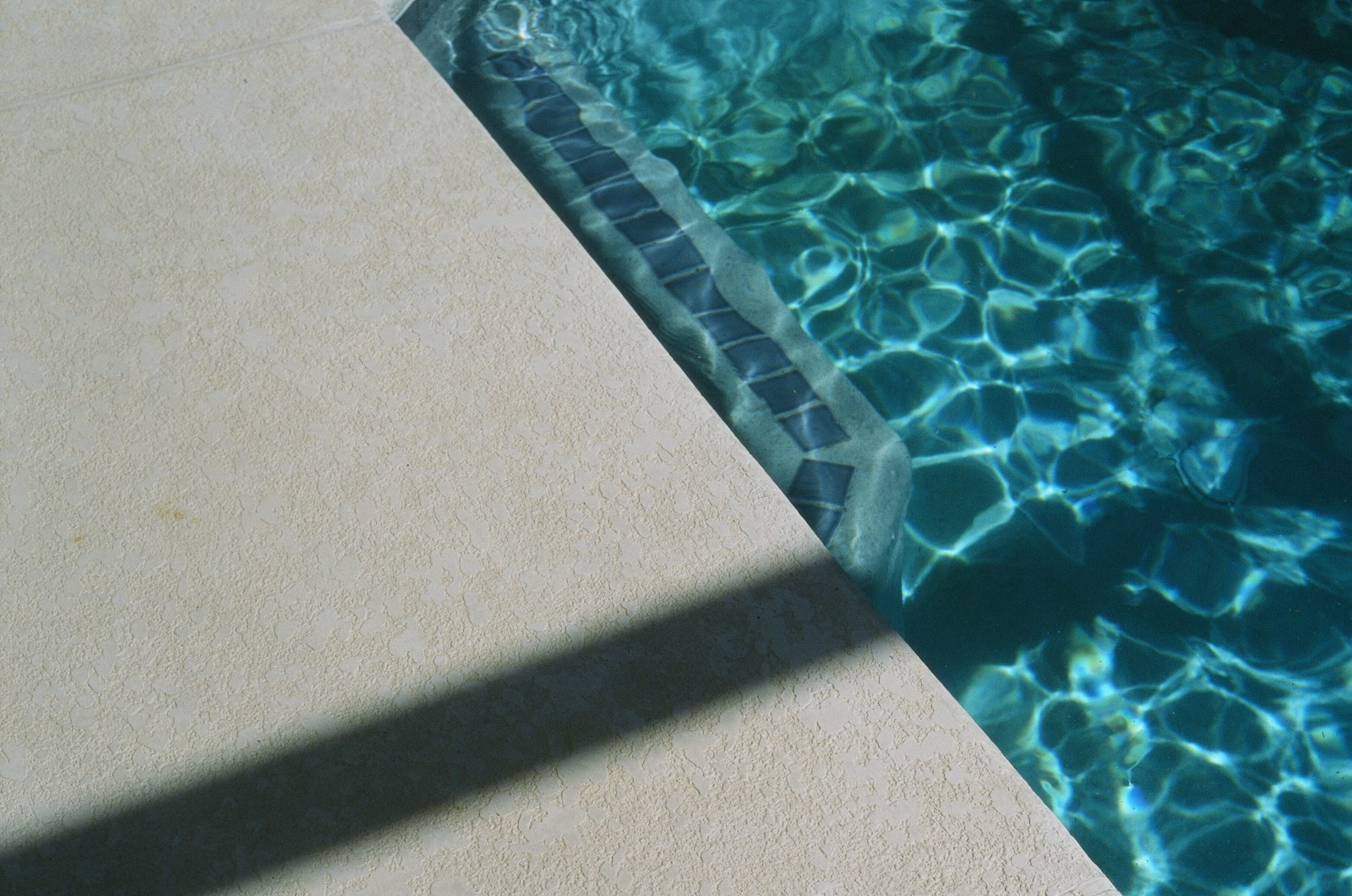 Sunlight rippling on pool water beside a pale stone deck.