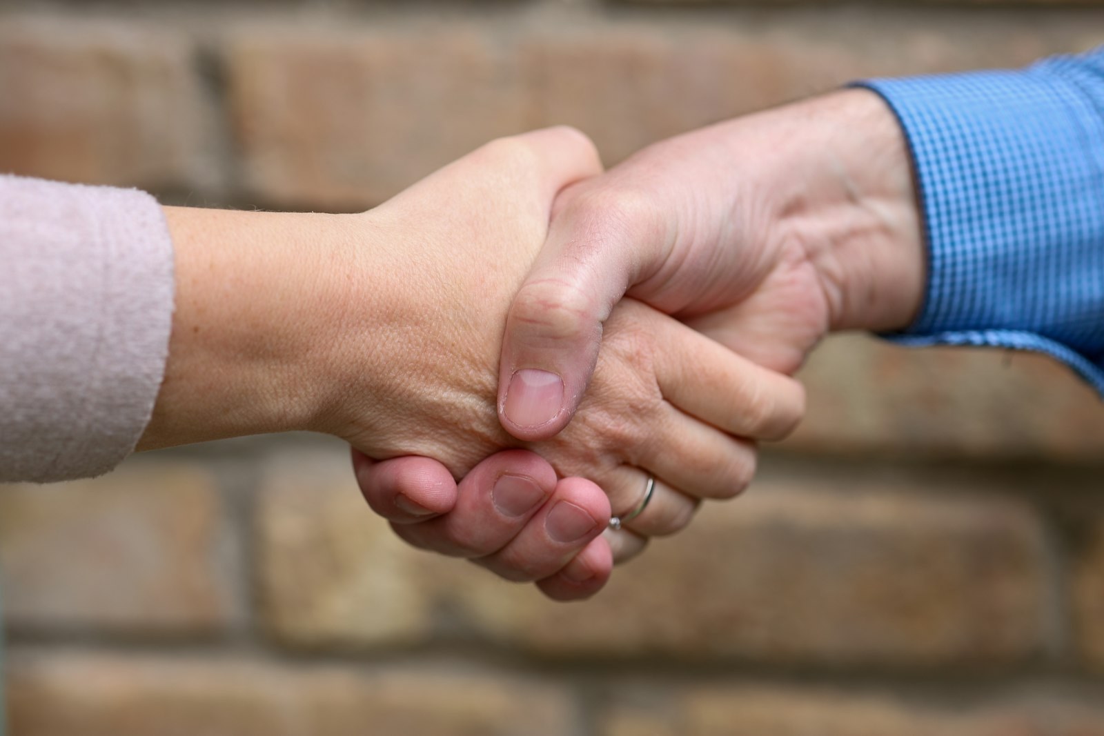 Two people shaking hands in front of a brick wall.