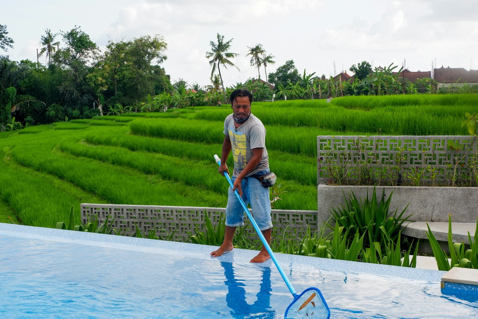 A man skimming a pool with a long-handled net.