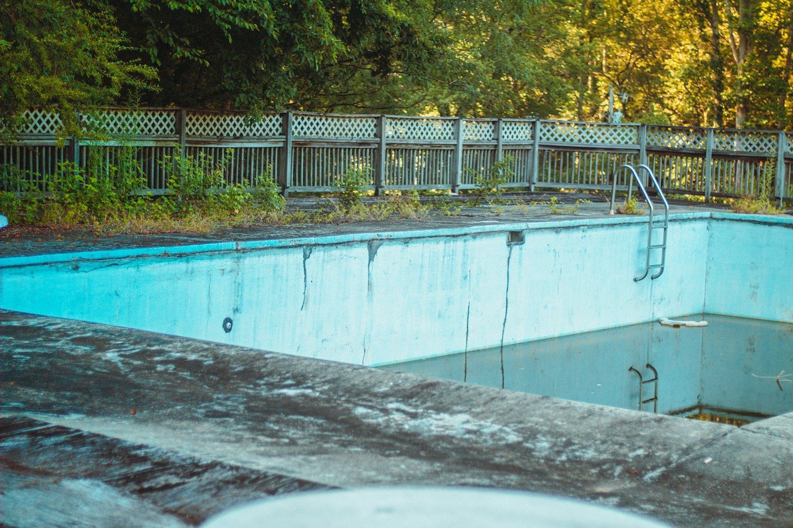 A drained swimming pool with stained walls and a ladder.