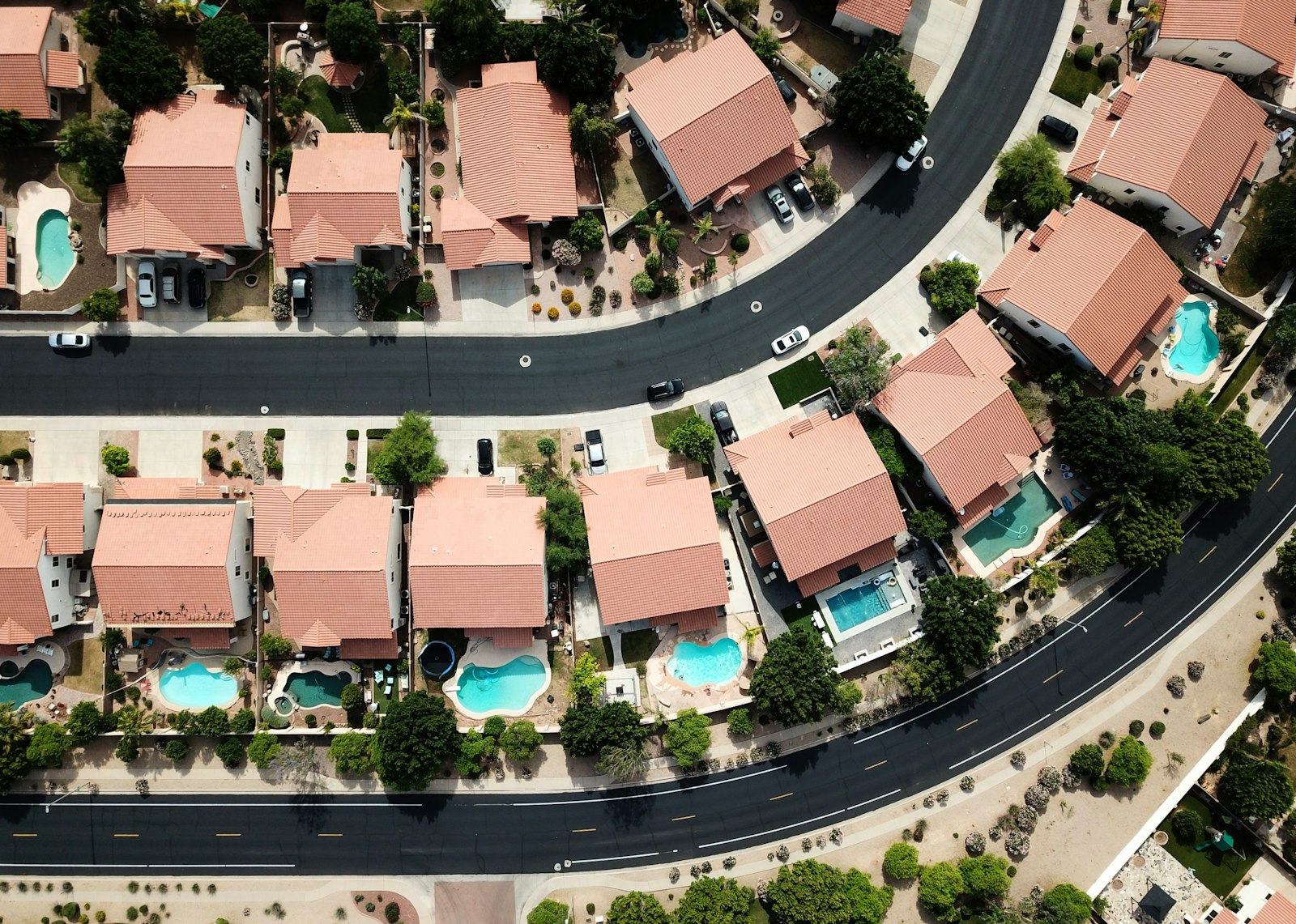 A suburban neighborhood seen from the air, with a pool behind most of the houses.