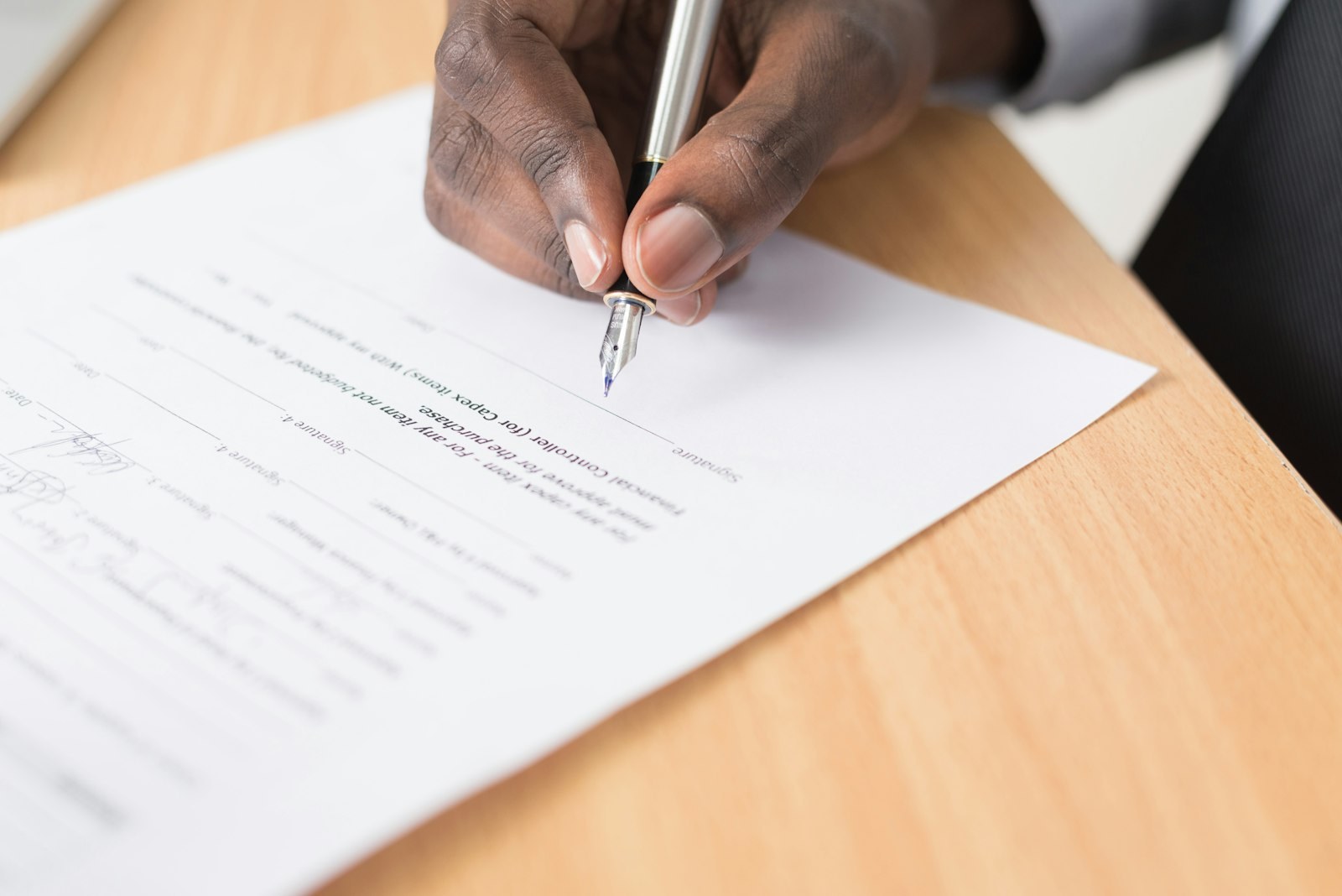A hand signing a printed document with a pen.
