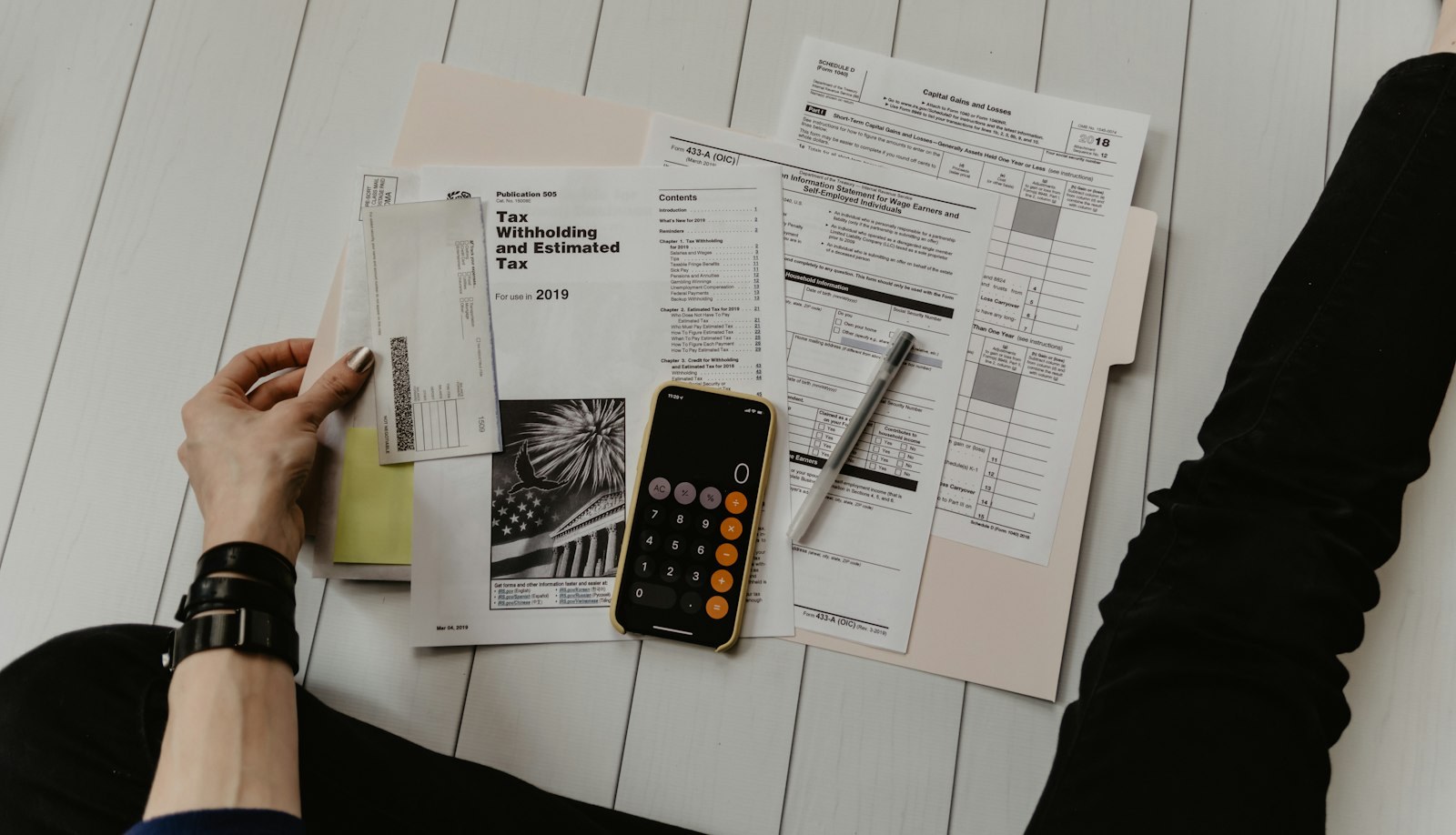 Tax forms, a pen and a phone calculator laid out on the floor, with a hand sorting receipts.