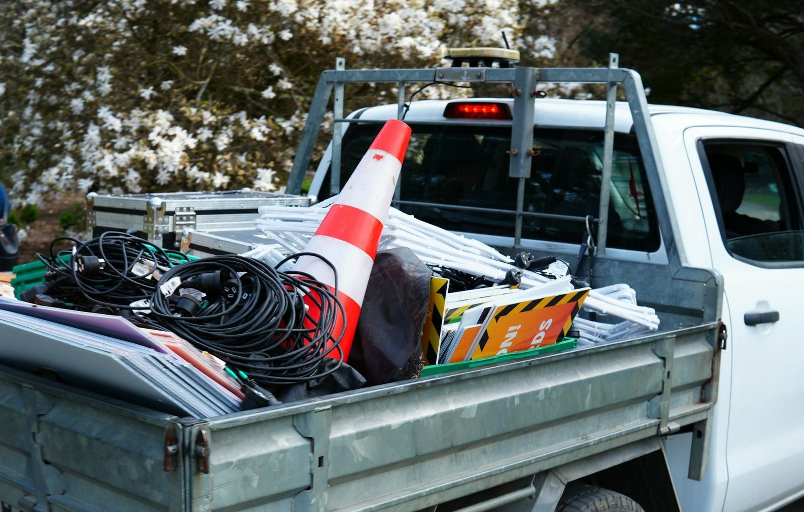 The bed of a white work truck loaded with coiled cable, a traffic cone and signs.