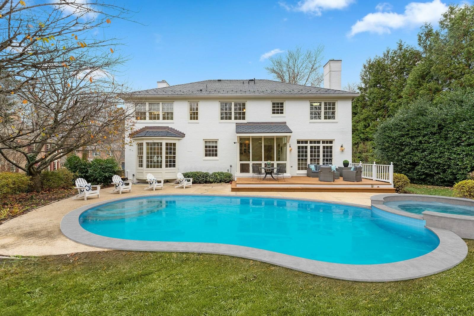 A white two-story house with a curved pool in the backyard.