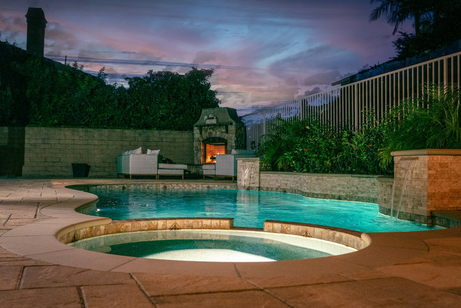 A backyard pool and spa lit up at dusk.