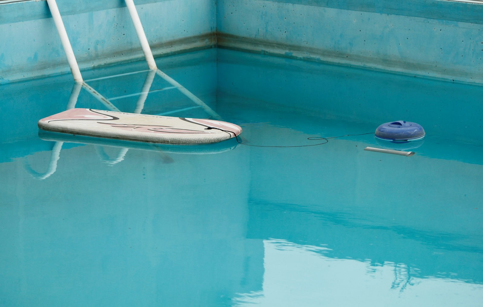 Hazy pool water with a chlorine floater and a bodyboard drifting on it.