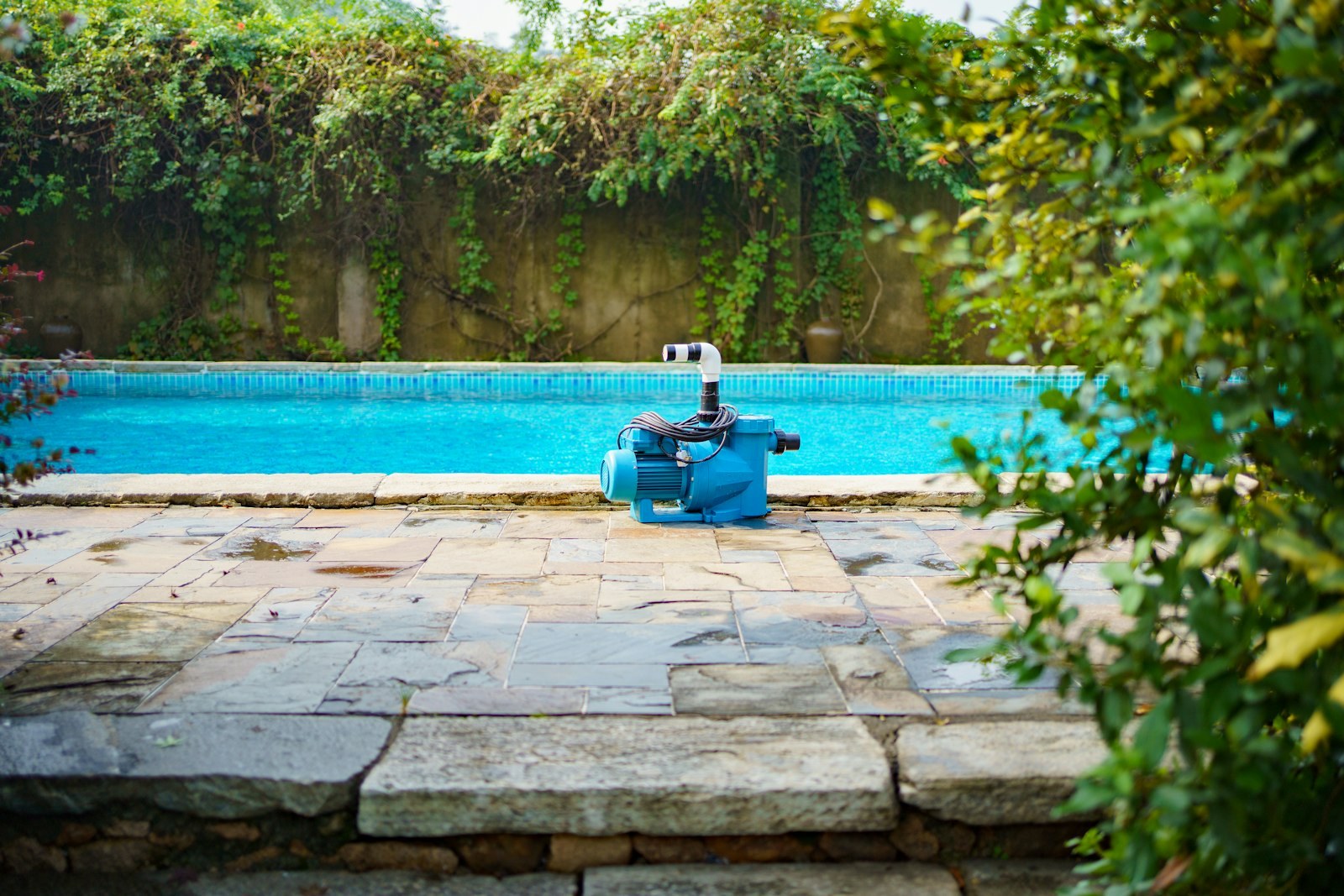 A small blue pump sitting on the stone deck beside a swimming pool.