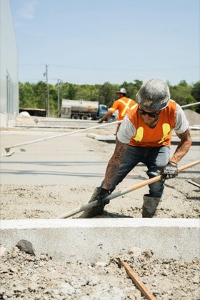 A worker in an orange vest shovelling concrete on a job site.