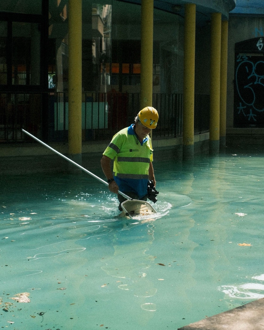 A worker in a hard hat standing in a shallow pool, clearing it with a net.