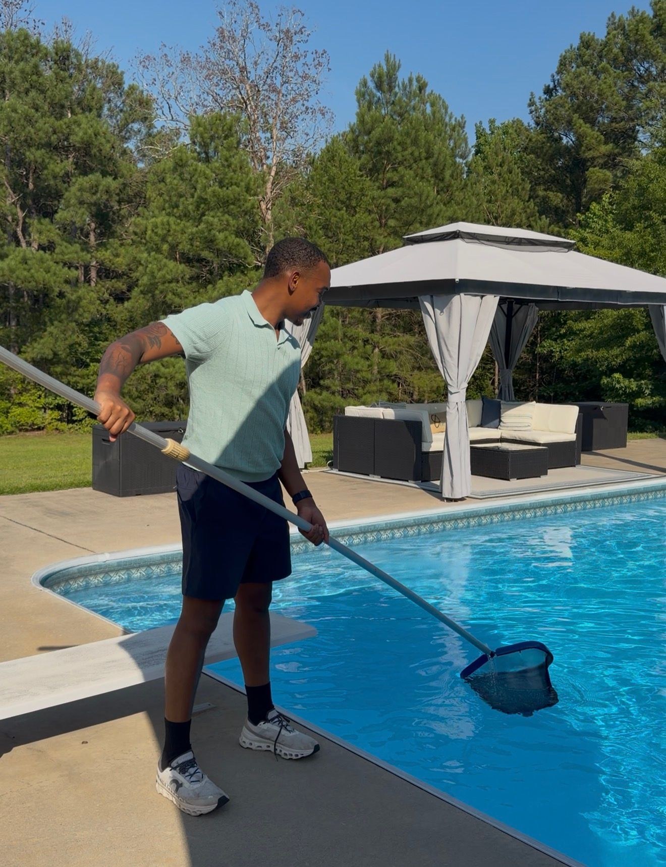 A pool technician skimming a backyard pool with a net.