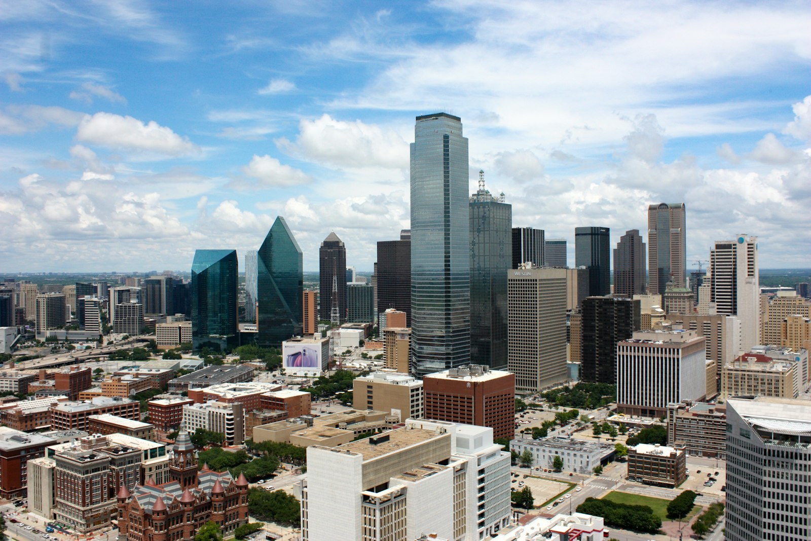 Downtown Dallas skyscrapers under a wide, cloudy sky.